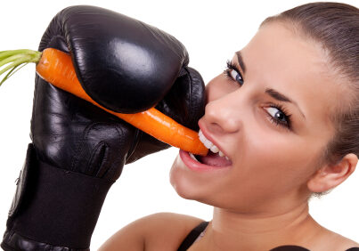 Young woman with boxing gloves biting raw carrot-close up