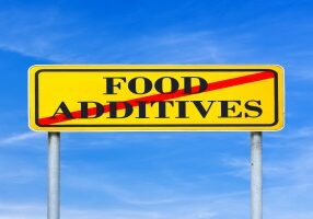 Food additives prohibited - conceptual image with the words Food additives crossed through in red on a yellow traffic sign against a sunny clear blue sky.