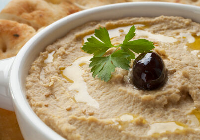 Hummus topped with olive oil, sesame seeds, parsley and an olive, served with Lebanese bread.