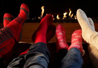 Four pairs feet in socks warming by fire