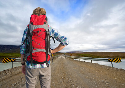 Tired Hiker , with a defeated pose, looks across a bridge at the bus home, leaving from the middle of nowhere.