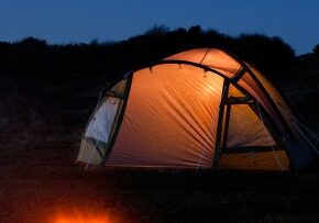 tent glows at night with campfire in front symbolizing camping holiday or vacation in the country