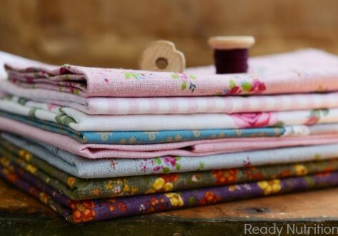 Pile of fabric with floral pattern in shabby chic style with wooden spools on top on wooden table