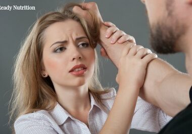 Young fair-haired woman holding man at his hand looking suppliantly at him while he grasps her hair. Isolated on grey background